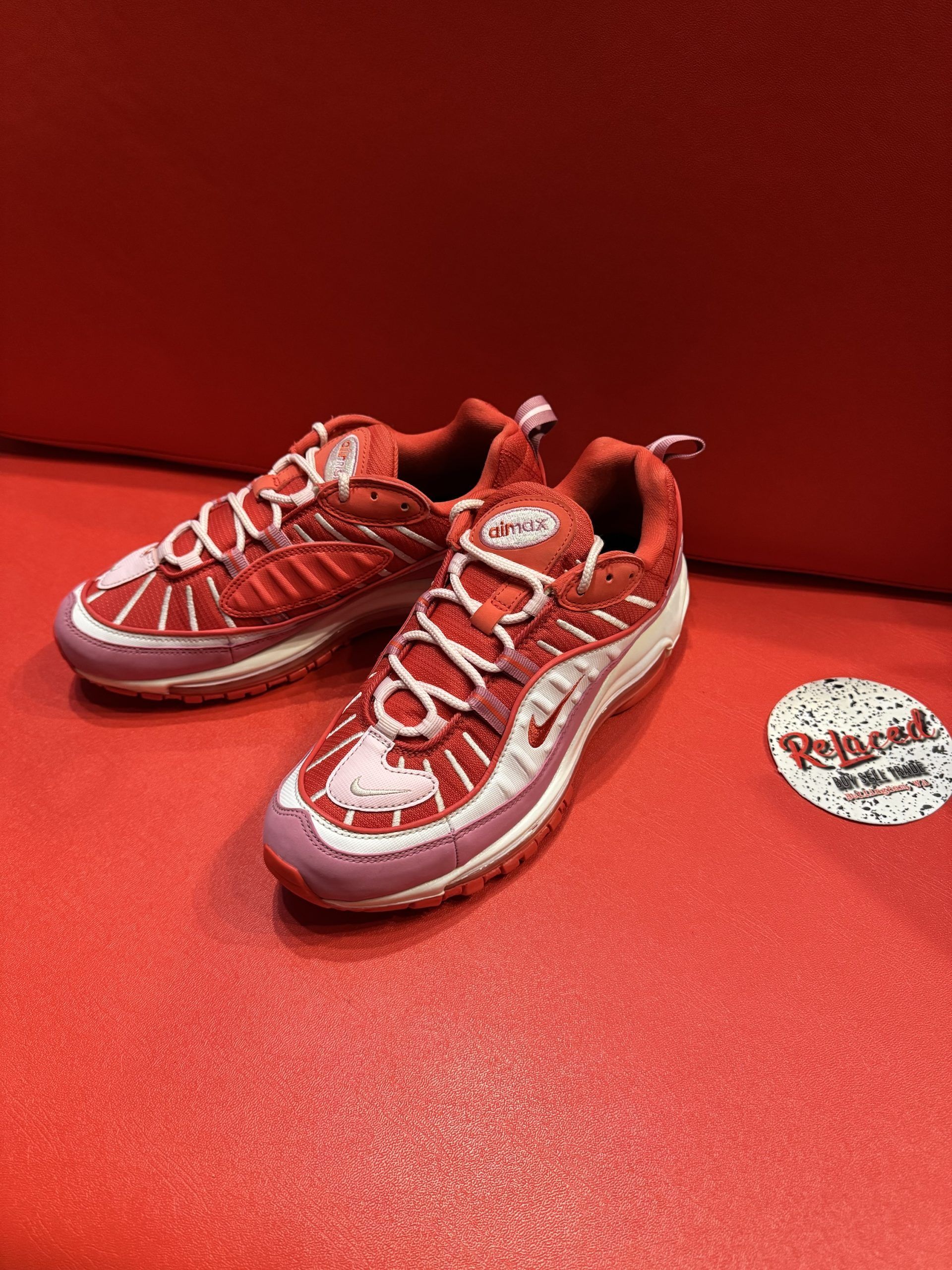 Red Nike Air Max 98 sneakers on a red surface, with a white and pink sole and laces.