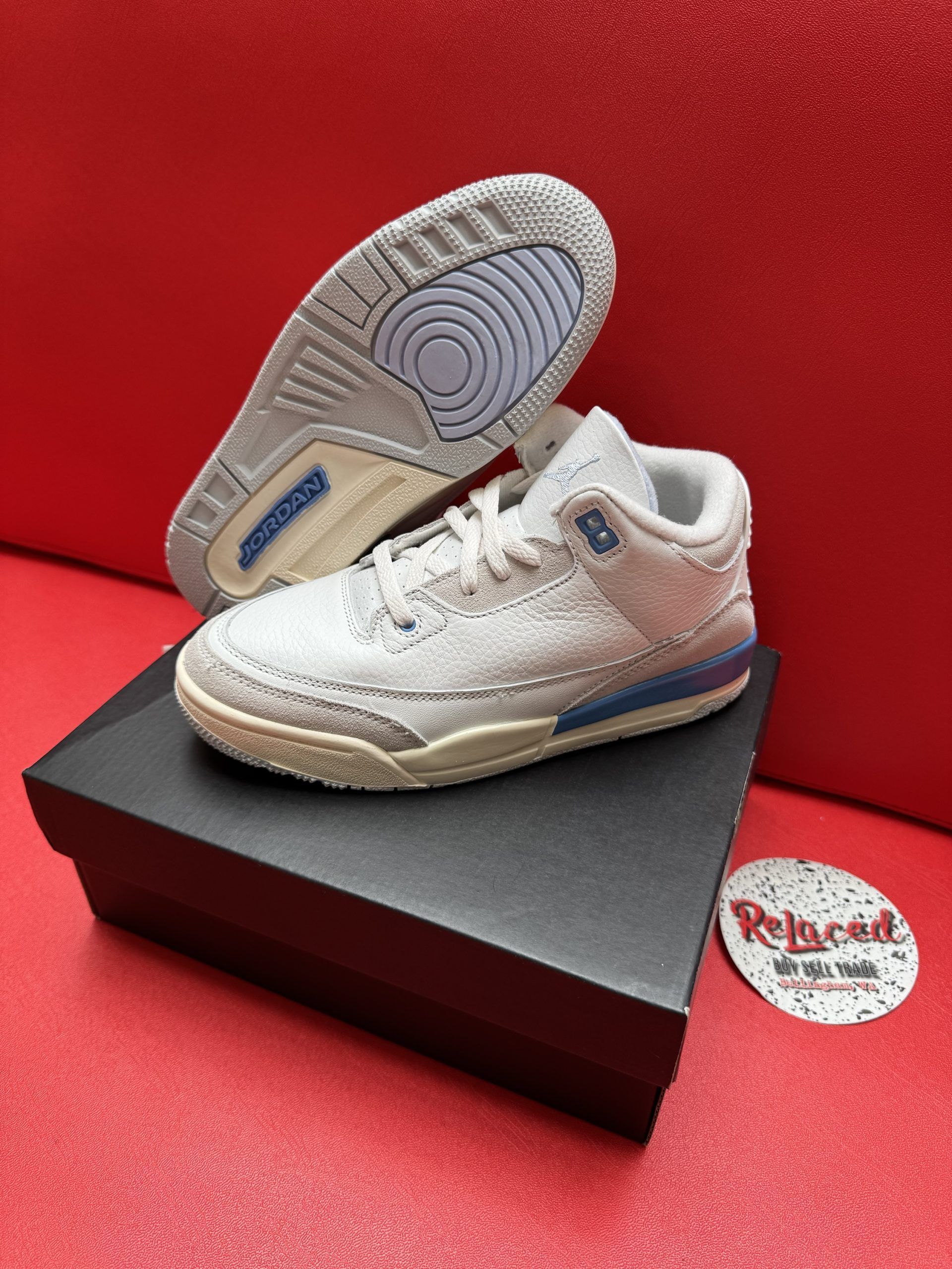 Air Jordan 3 sneakers, light grey, baby size, on a black box, with a red background.
