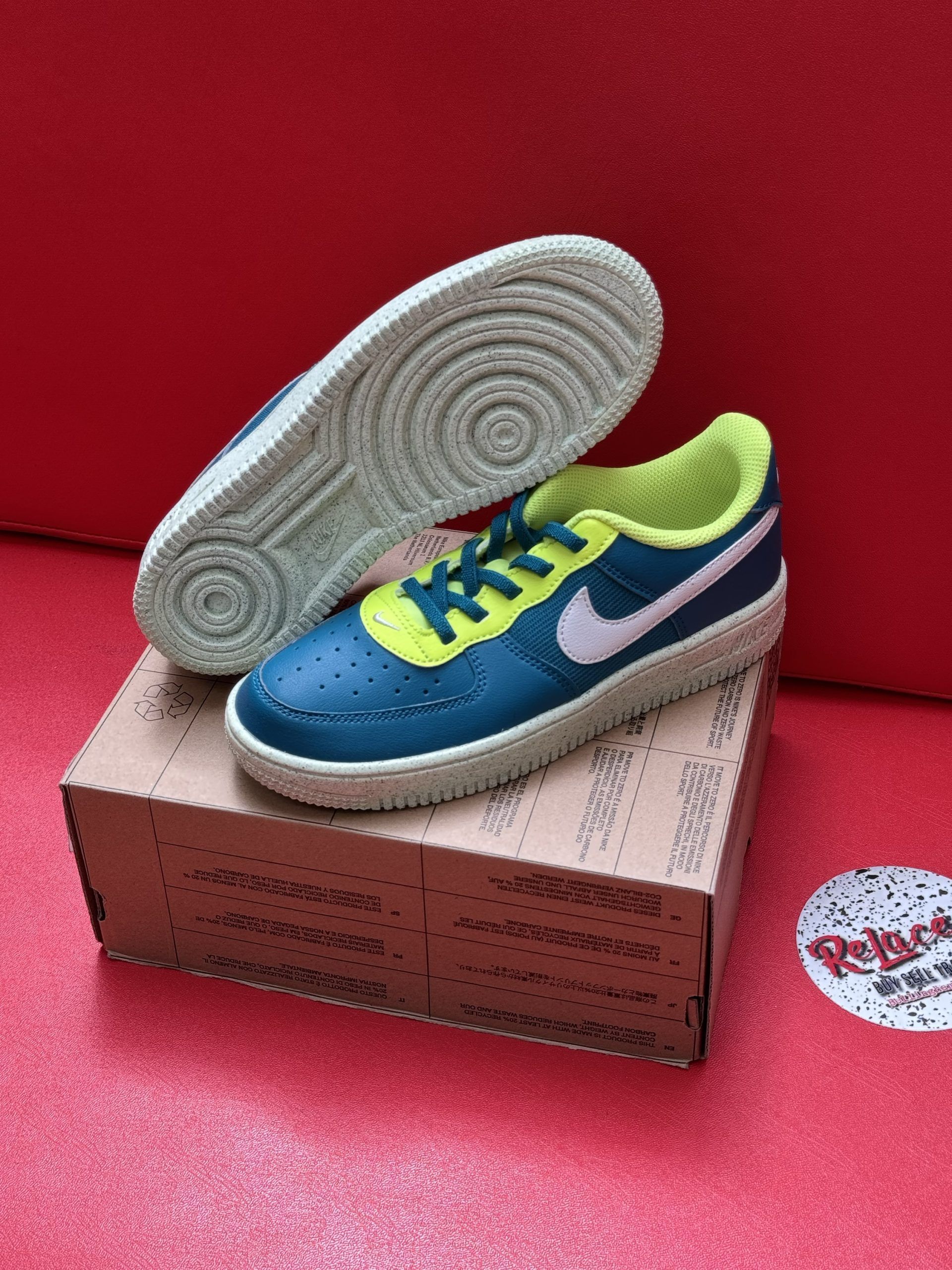 Blue and yellow Nike Air Force 1 sneakers with a beige sole, on top of a brown shoe box, against a red backdrop.