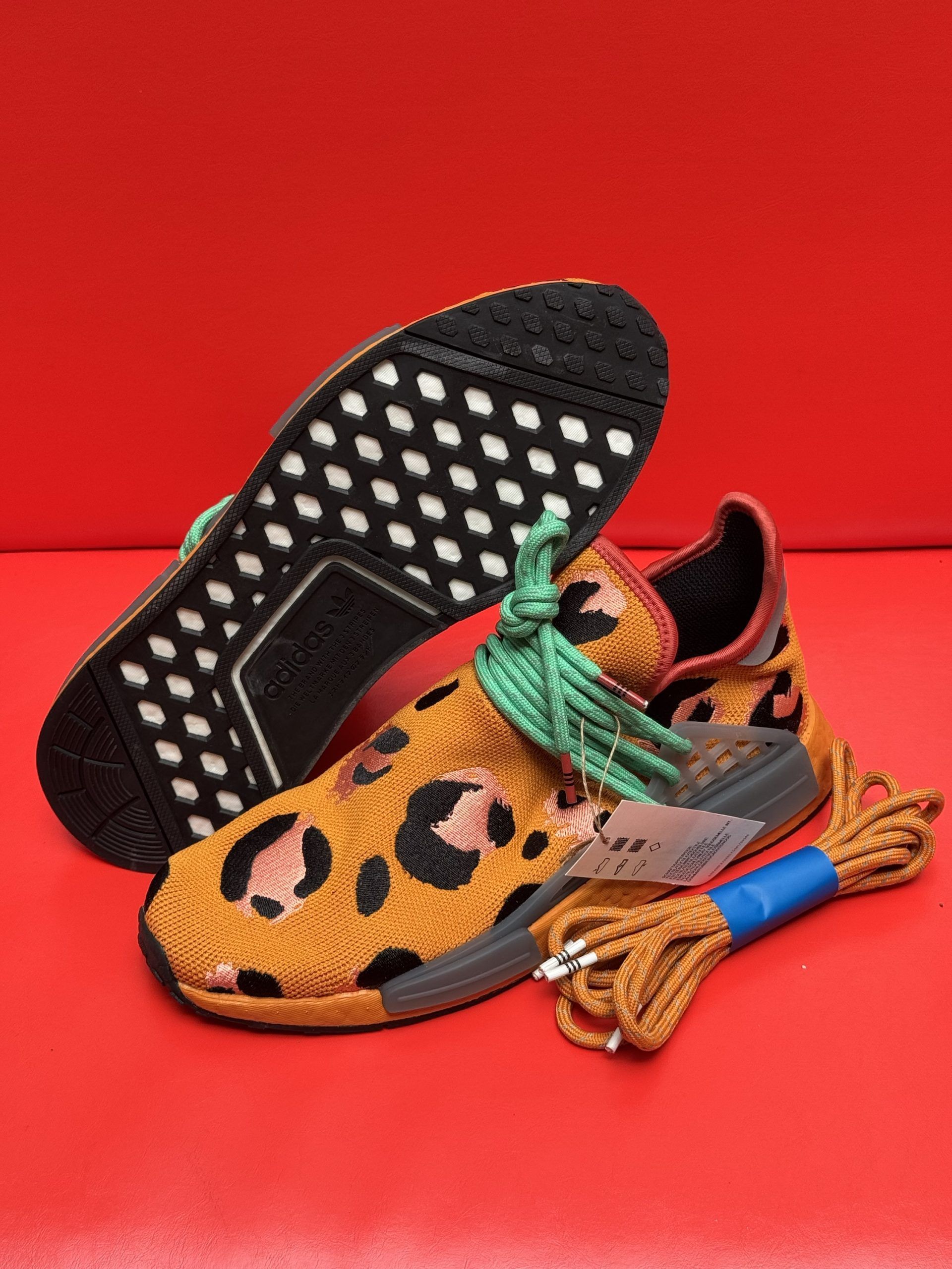 Leopard-print Adidas sneakers with extra brown and green laces on red background.