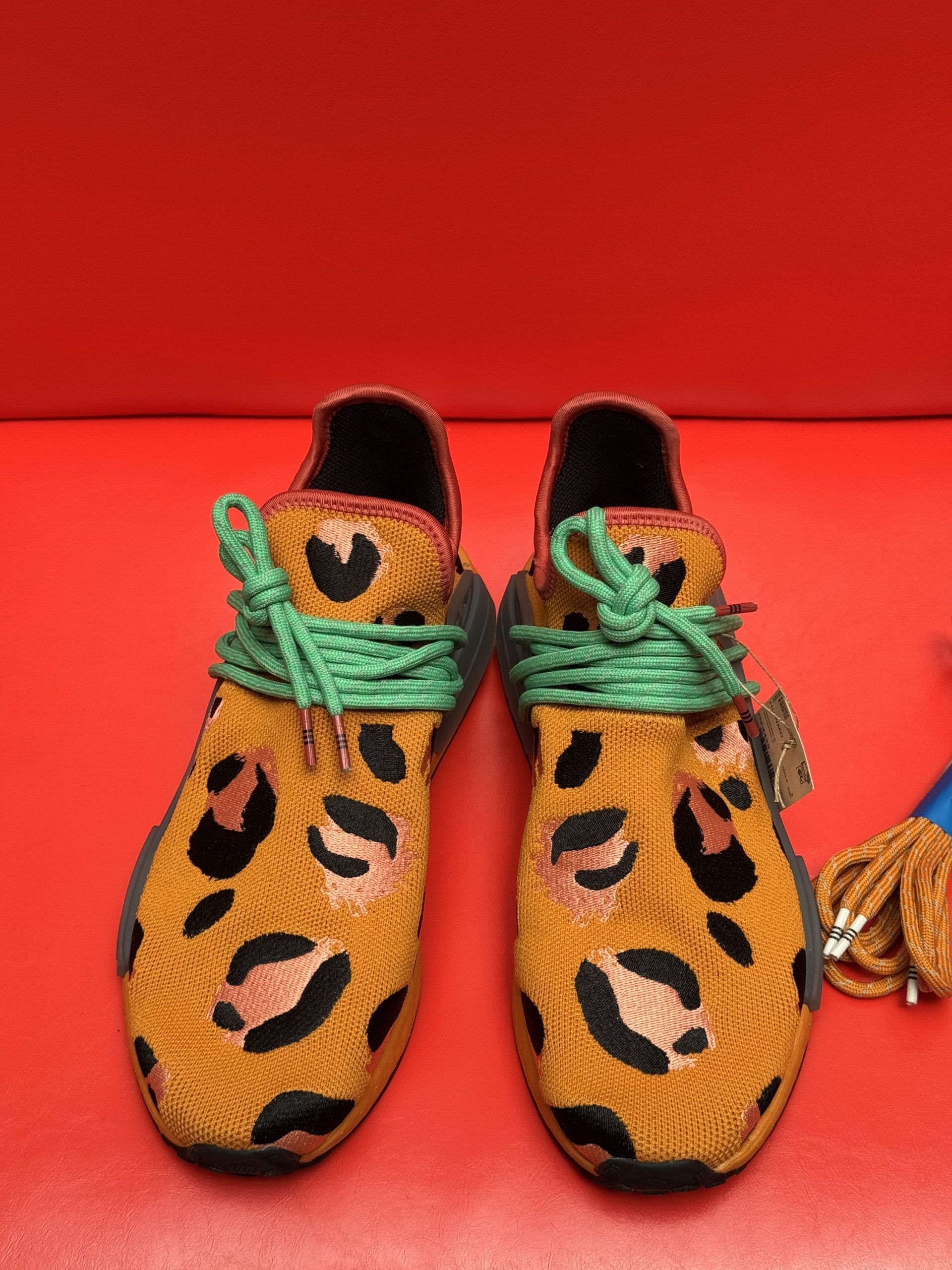 Leopard-print Adidas sneakers with extra brown and green laces on red background.