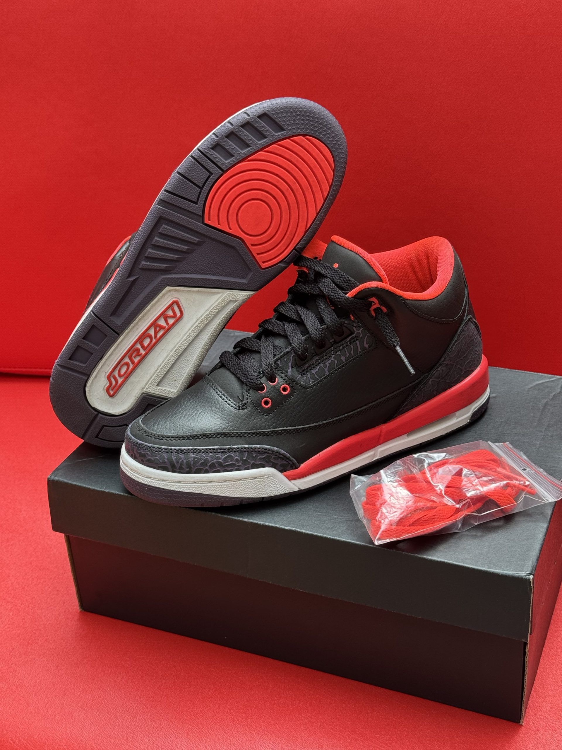Black and red Air Jordan 3 sneakers on a box, with extra laces and a red sole.