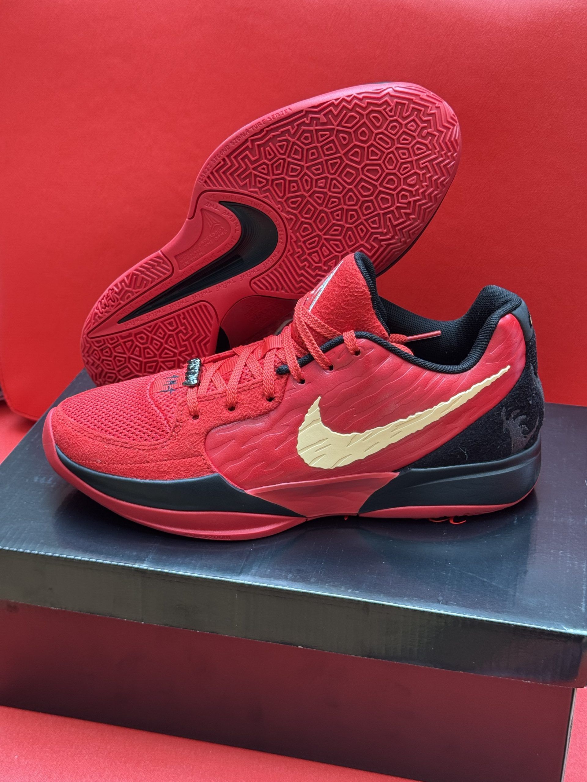 Red Nike basketball shoe with a gold swoosh, black accents, and a red sole on a black box.