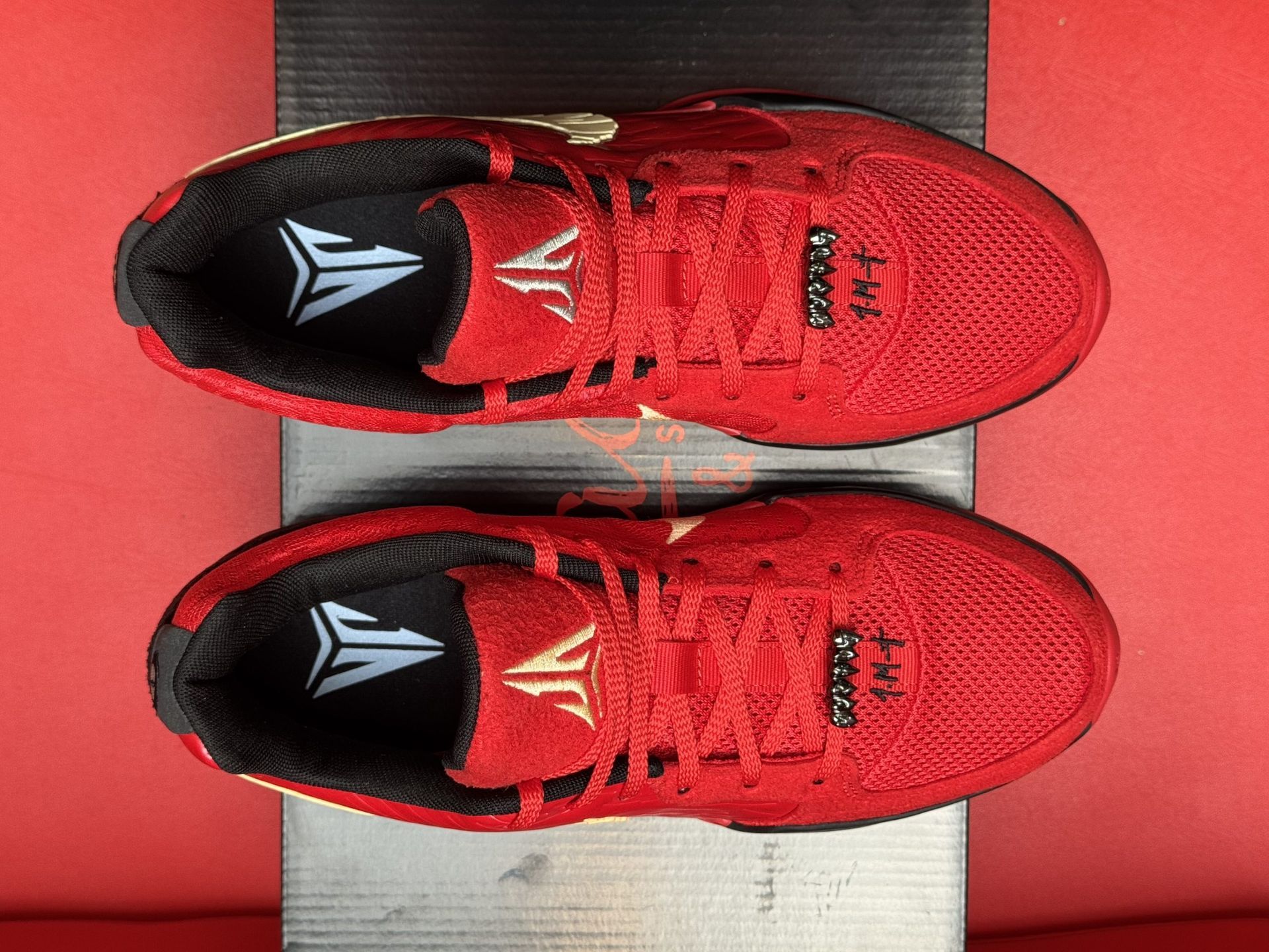 Red Nike basketball shoe with a gold swoosh, black accents, and a red sole on a black box.