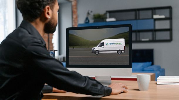 Person at desk viewing a white delivery van on a computer screen in an office.