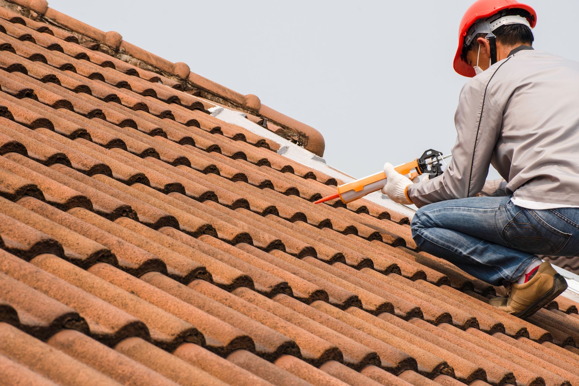 A roofer is using a glue gun with silicone adhesive to seal a leak on a roof.