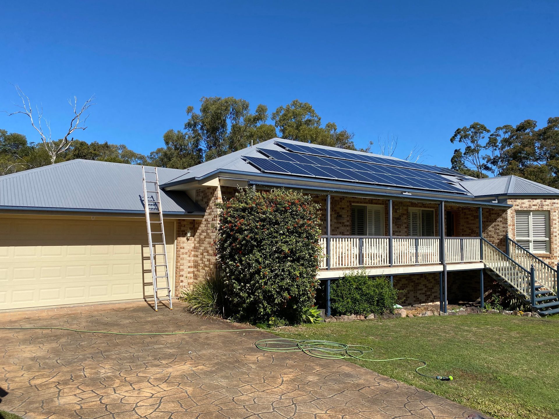 A house with solar panels on the roof, a ladder leaning against it, under a blue sky.