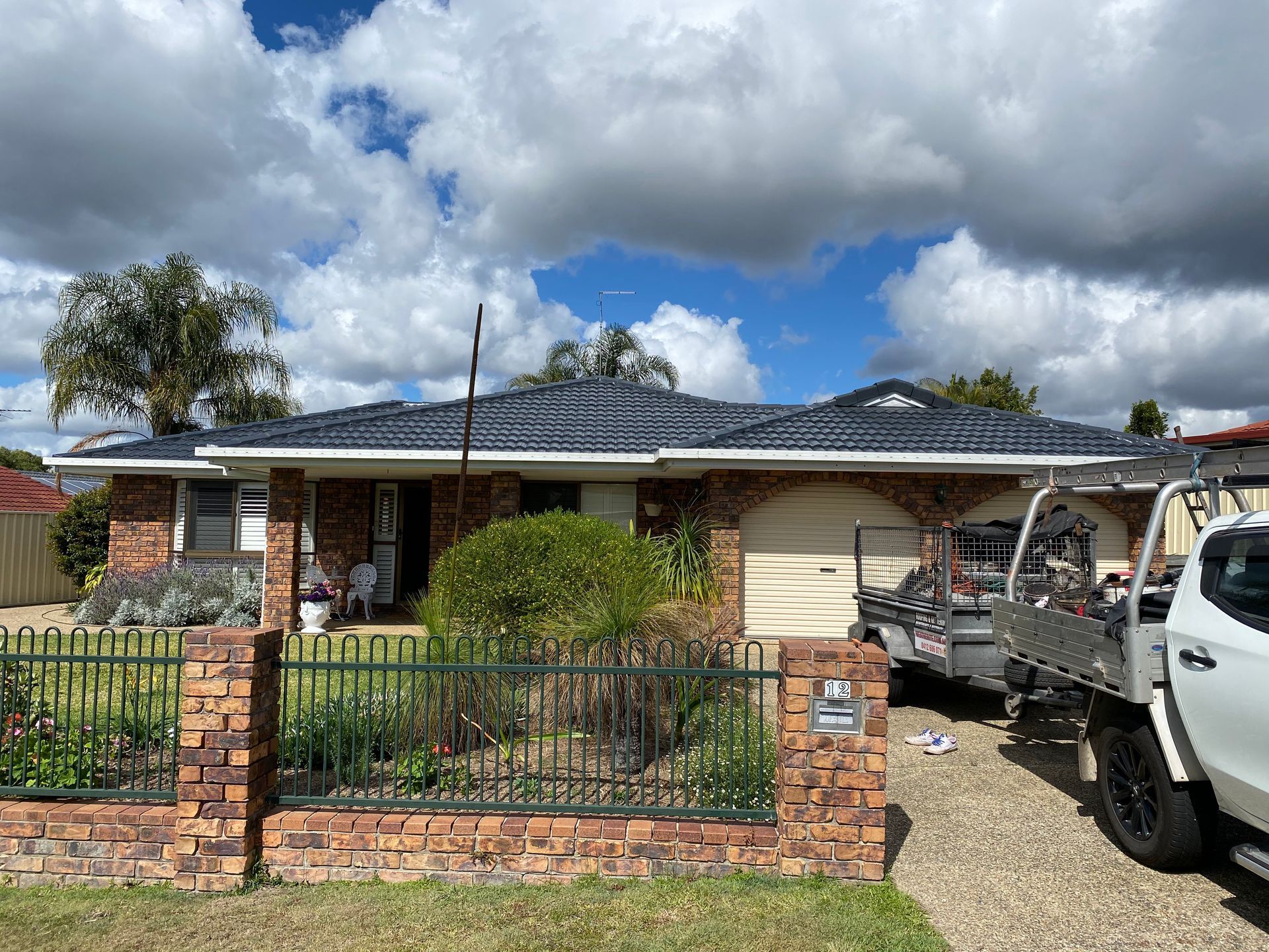 Brick house with a dark blue tiled roof, cloudy sky, and a white truck parked in the driveway.