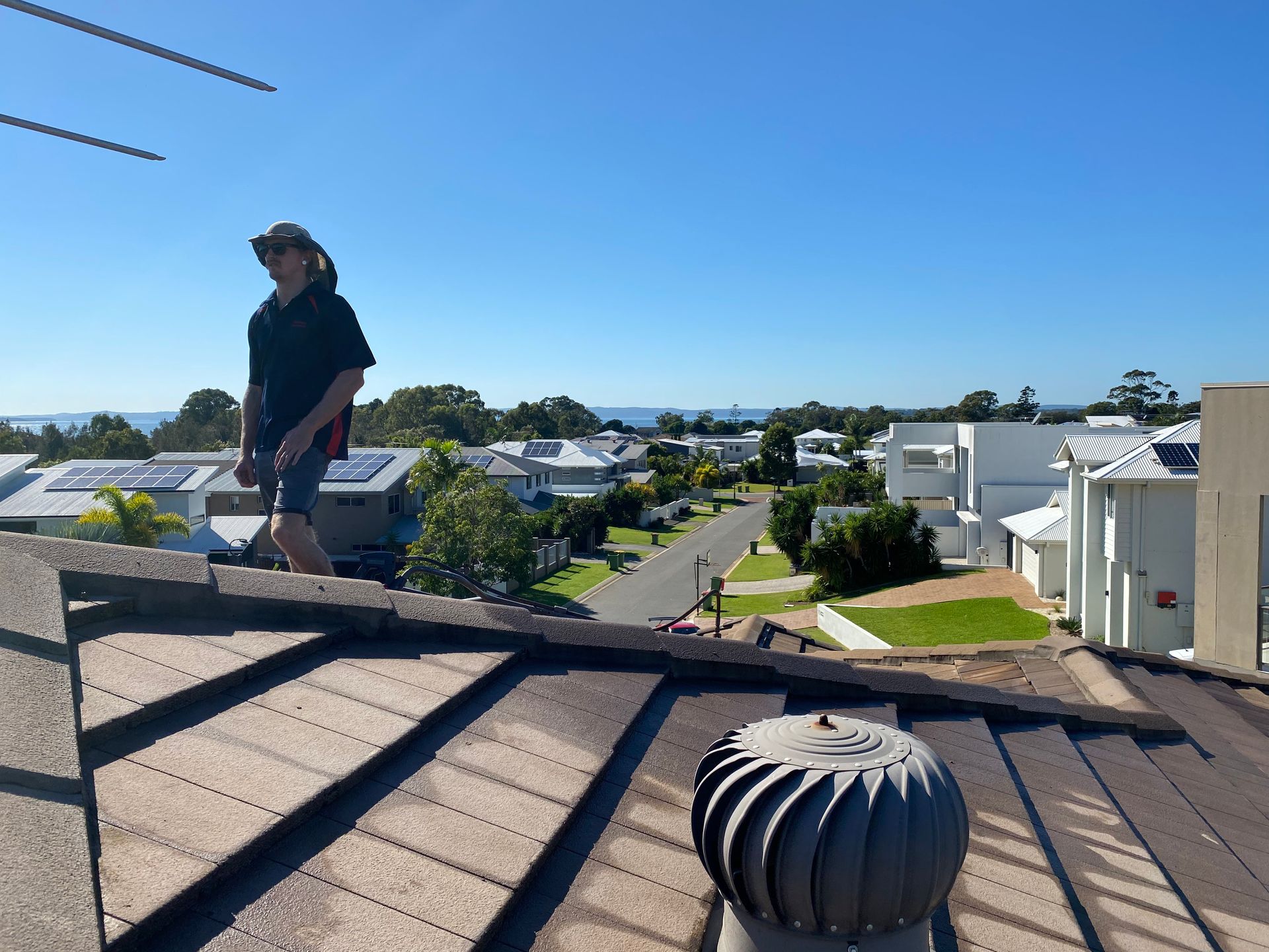 Person on rooftop with suburban view, sunny day.