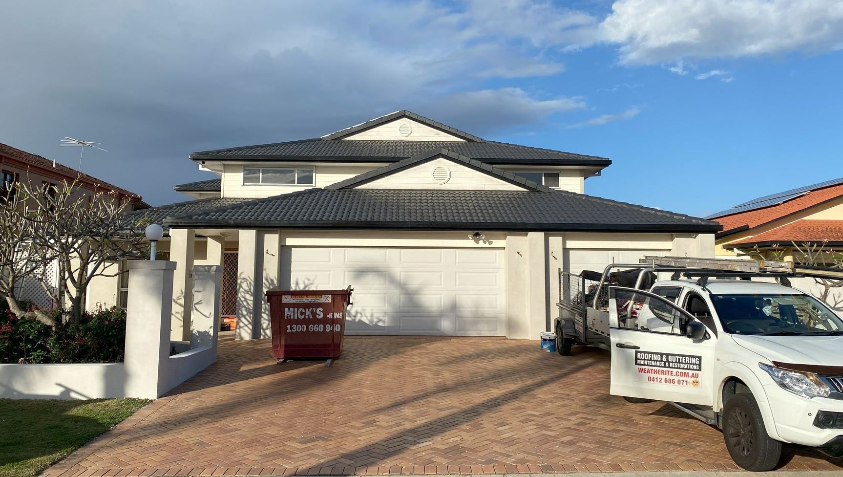 Two-story house with black roof, white garage doors, red driveway, and white truck parked in front.