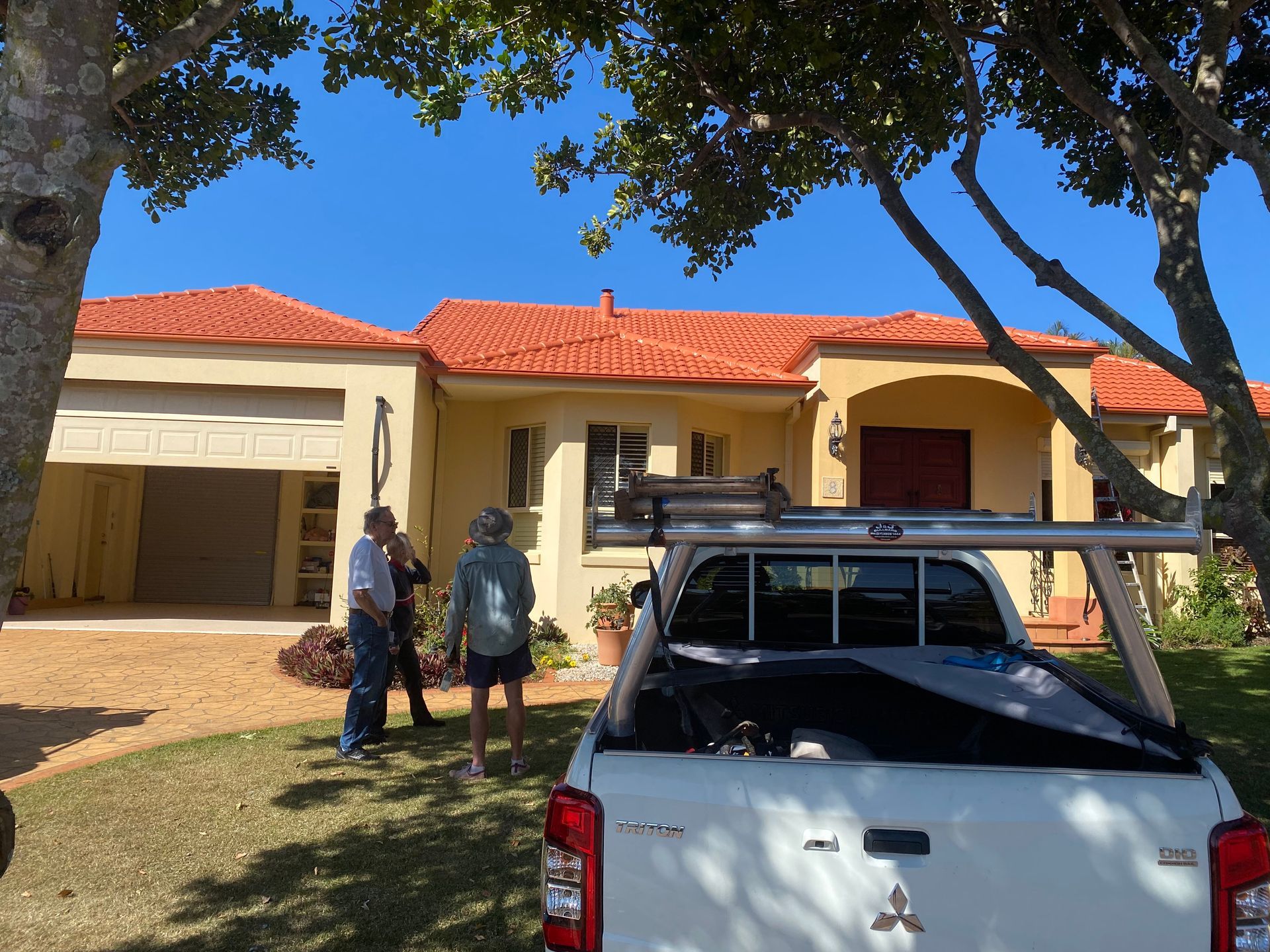 People standing outside a yellow house with an orange tile roof, next to a white truck.