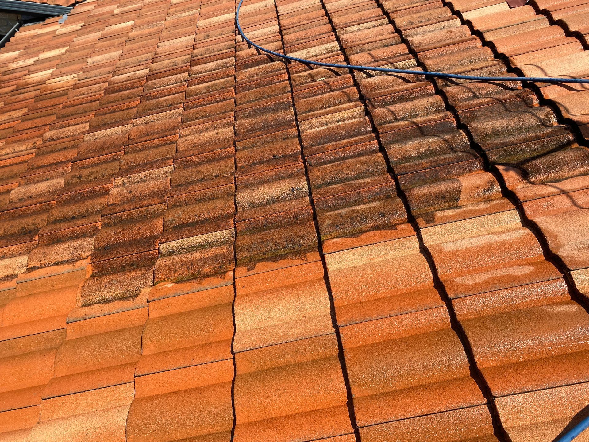 Terracotta tile roof being cleaned with visible lines showing dirt removal.