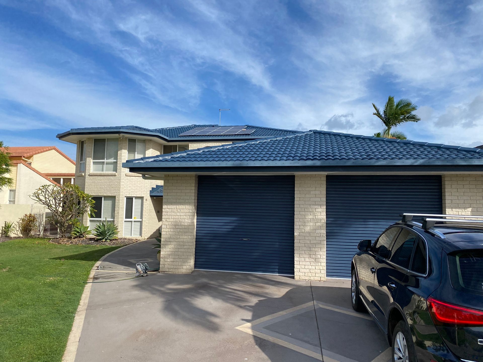 Two-story house with blue roof and garage doors. Black SUV parked in driveway on a sunny day.