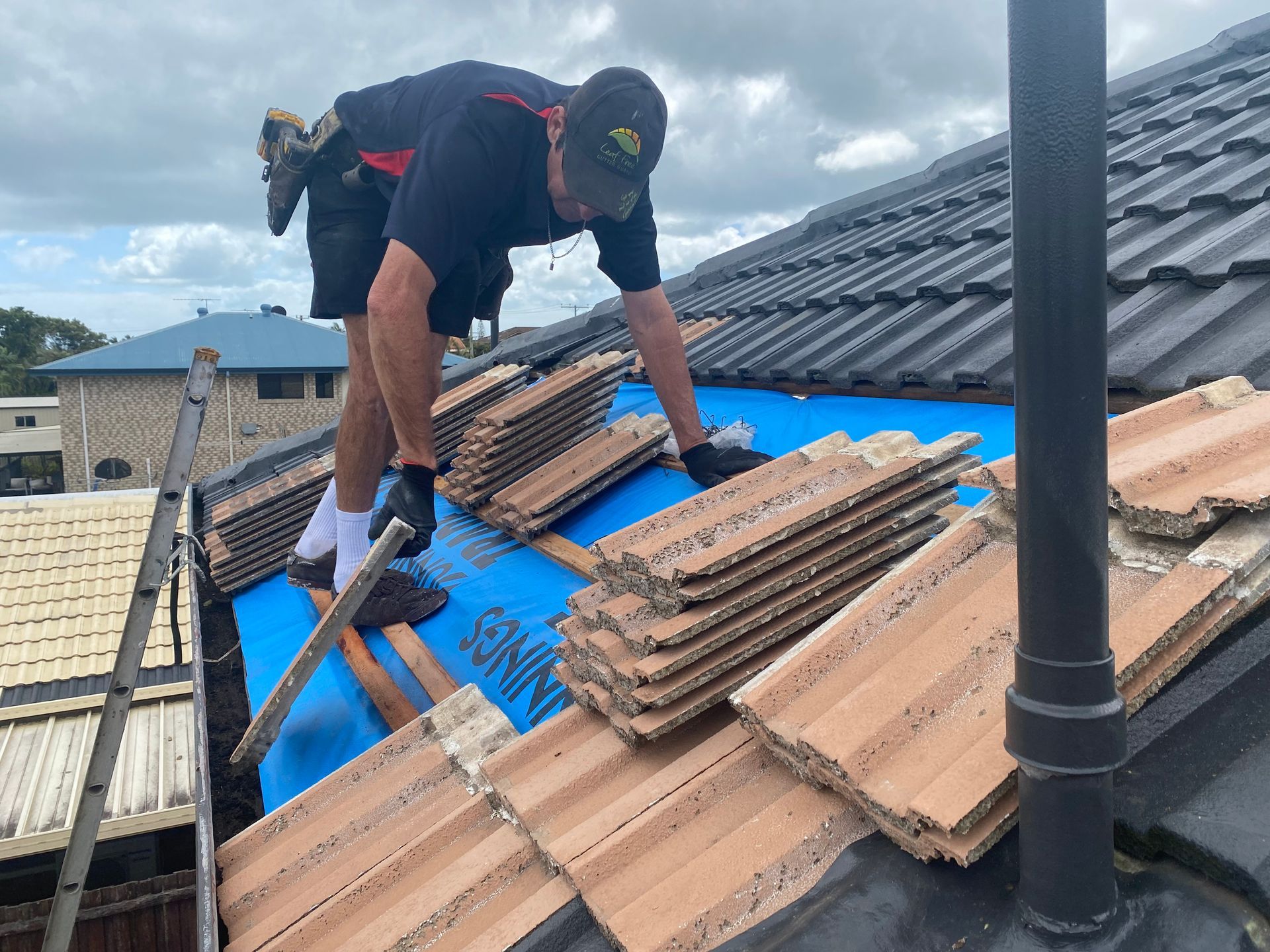Roofer on a tiled roof, installing tiles over blue underlayment, sunny day.