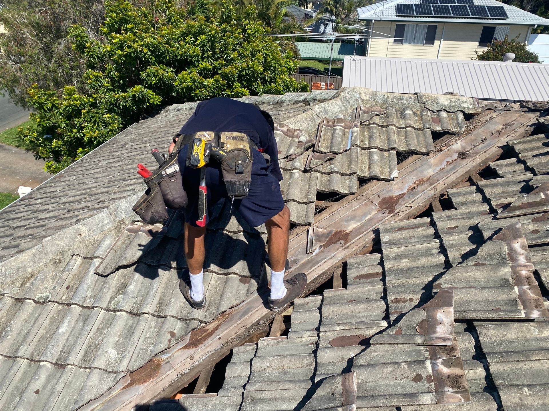 Roofer on a damaged tile roof, with tools, outdoors.