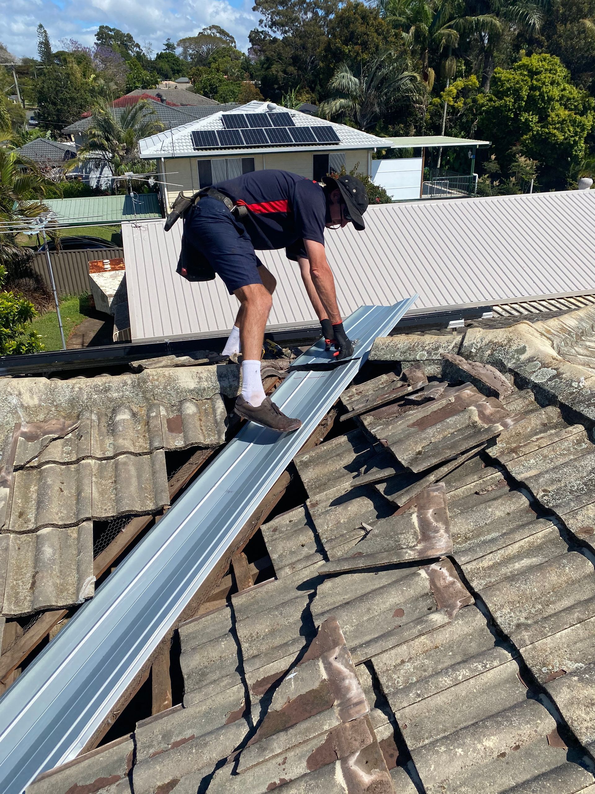 A worker on a roof installing a metal strip, surrounded by old tiles. Sunny day.