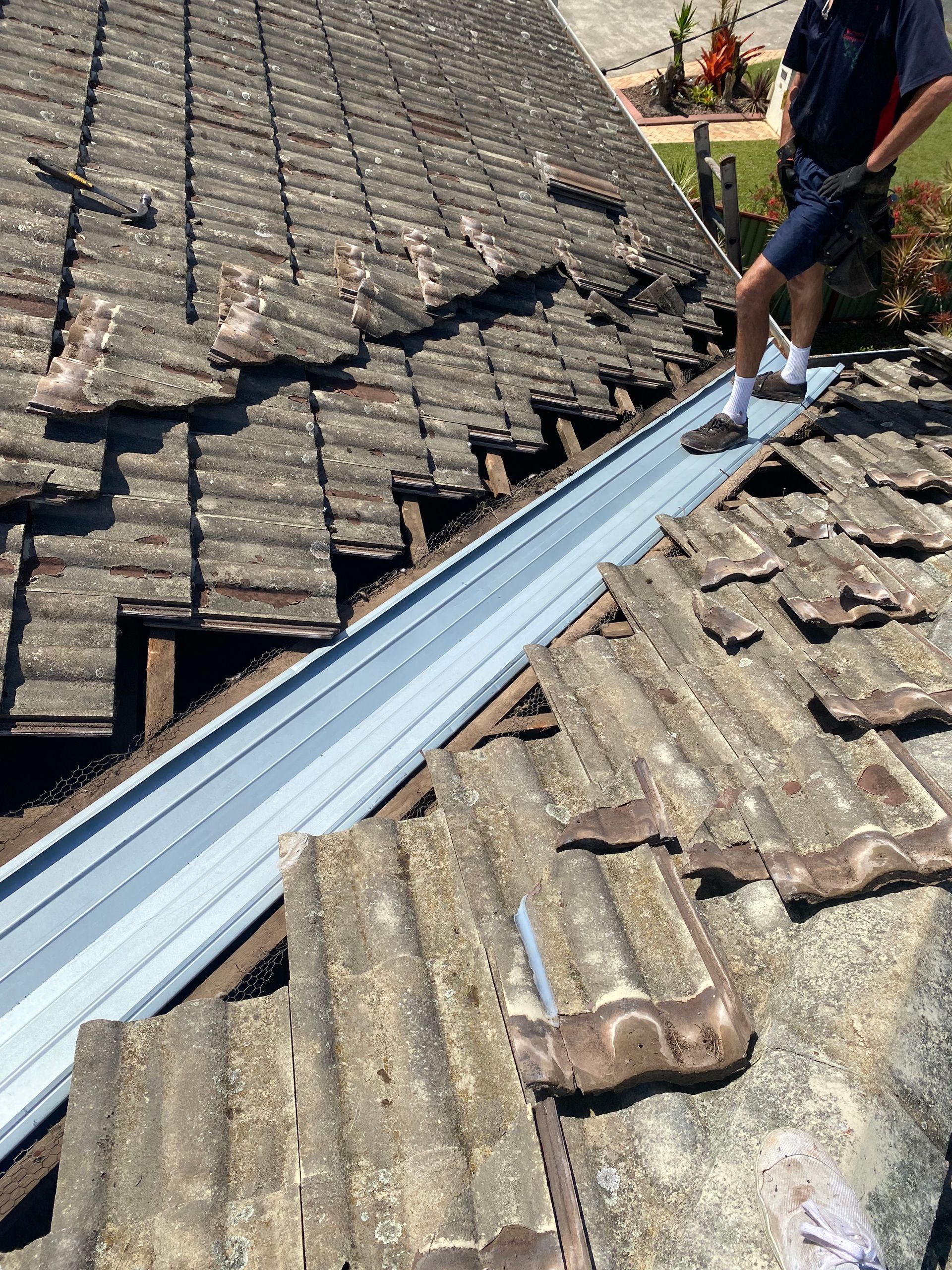 Person on roof, damaged tiles, showing new gutter, repairs in progress.