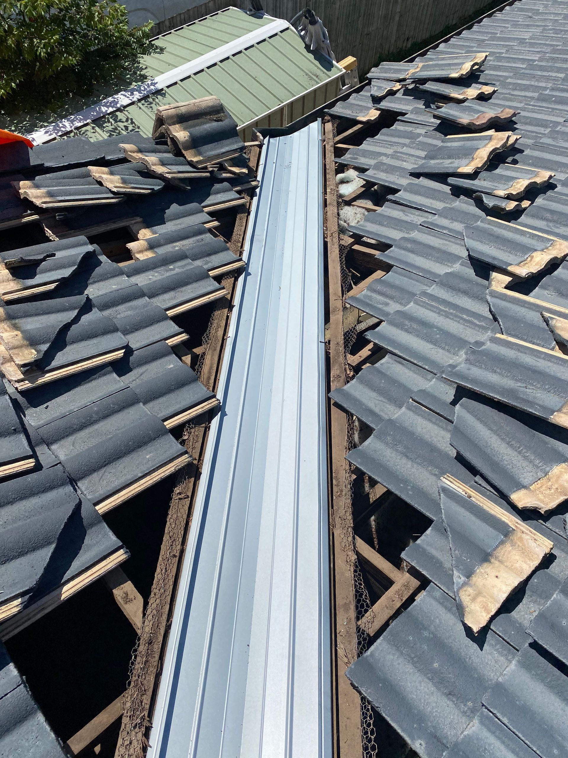 Roof tiles removed, revealing metal valley flashing. Construction work in progress.