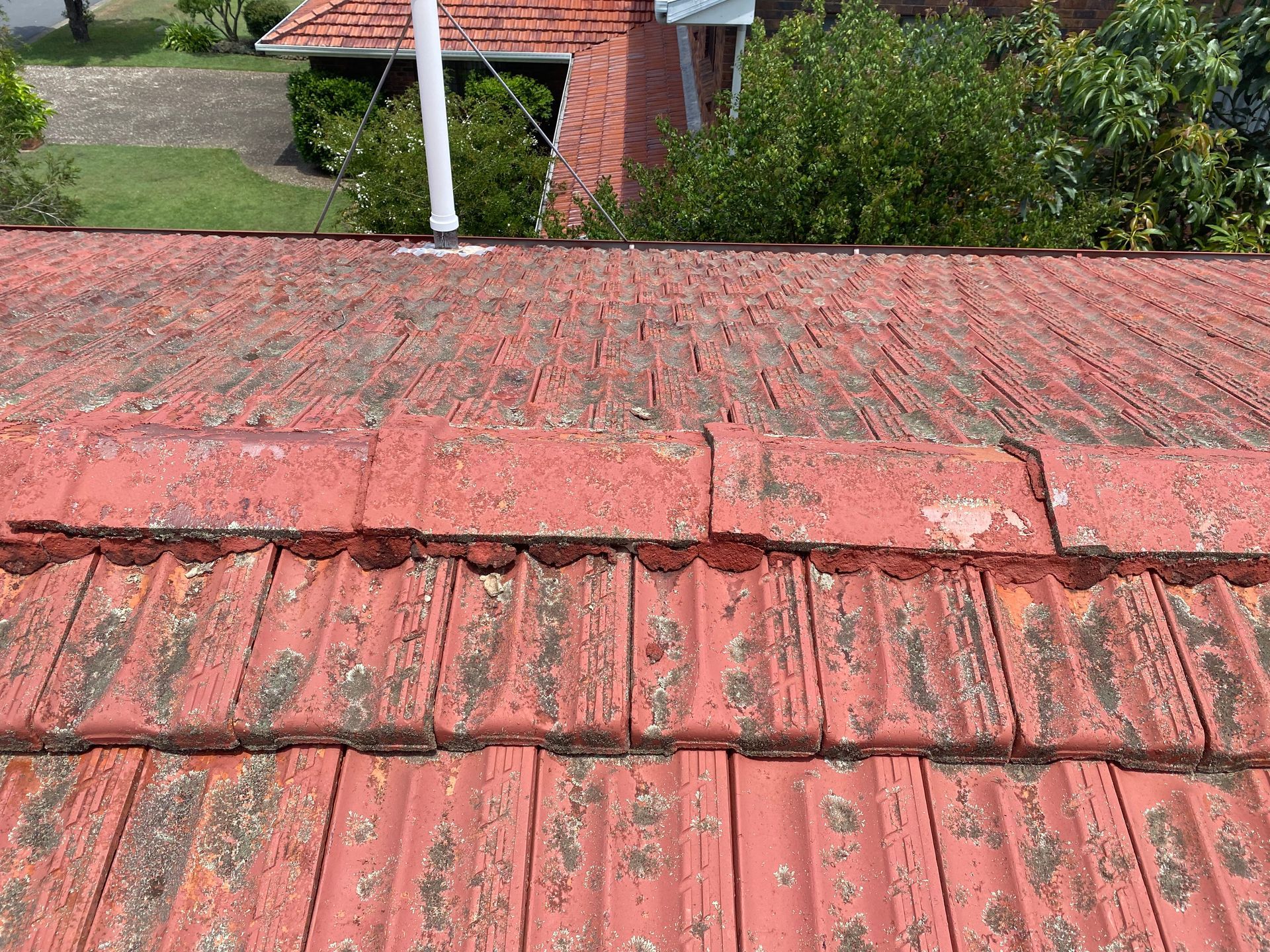 Red tiled roof, weathered and showing algae growth, with a white pipe visible.