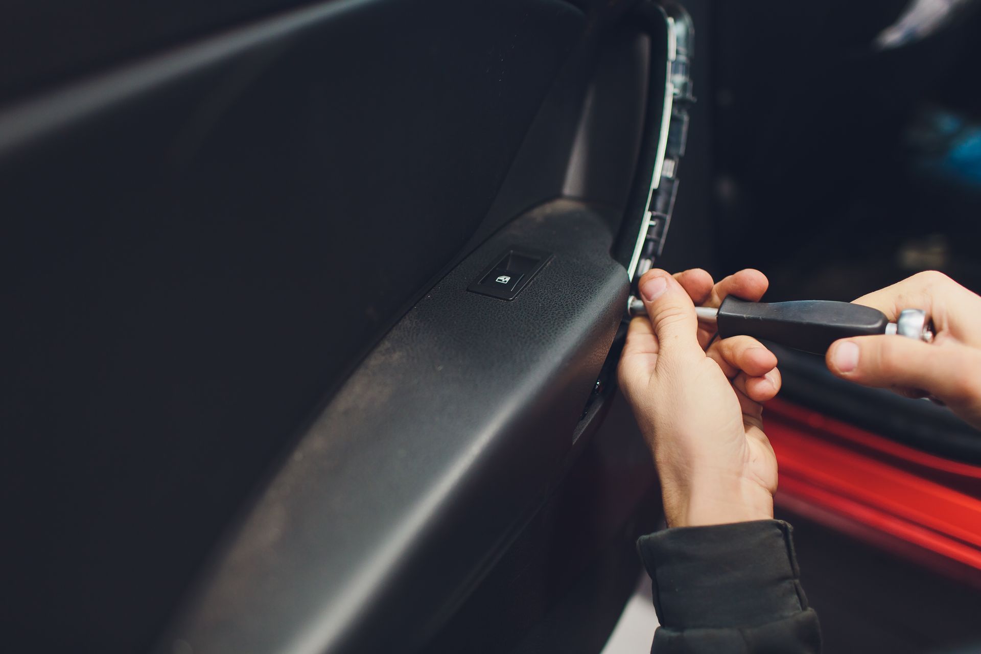 Person using a screwdriver to work on a car door panel, likely removing or installing it.