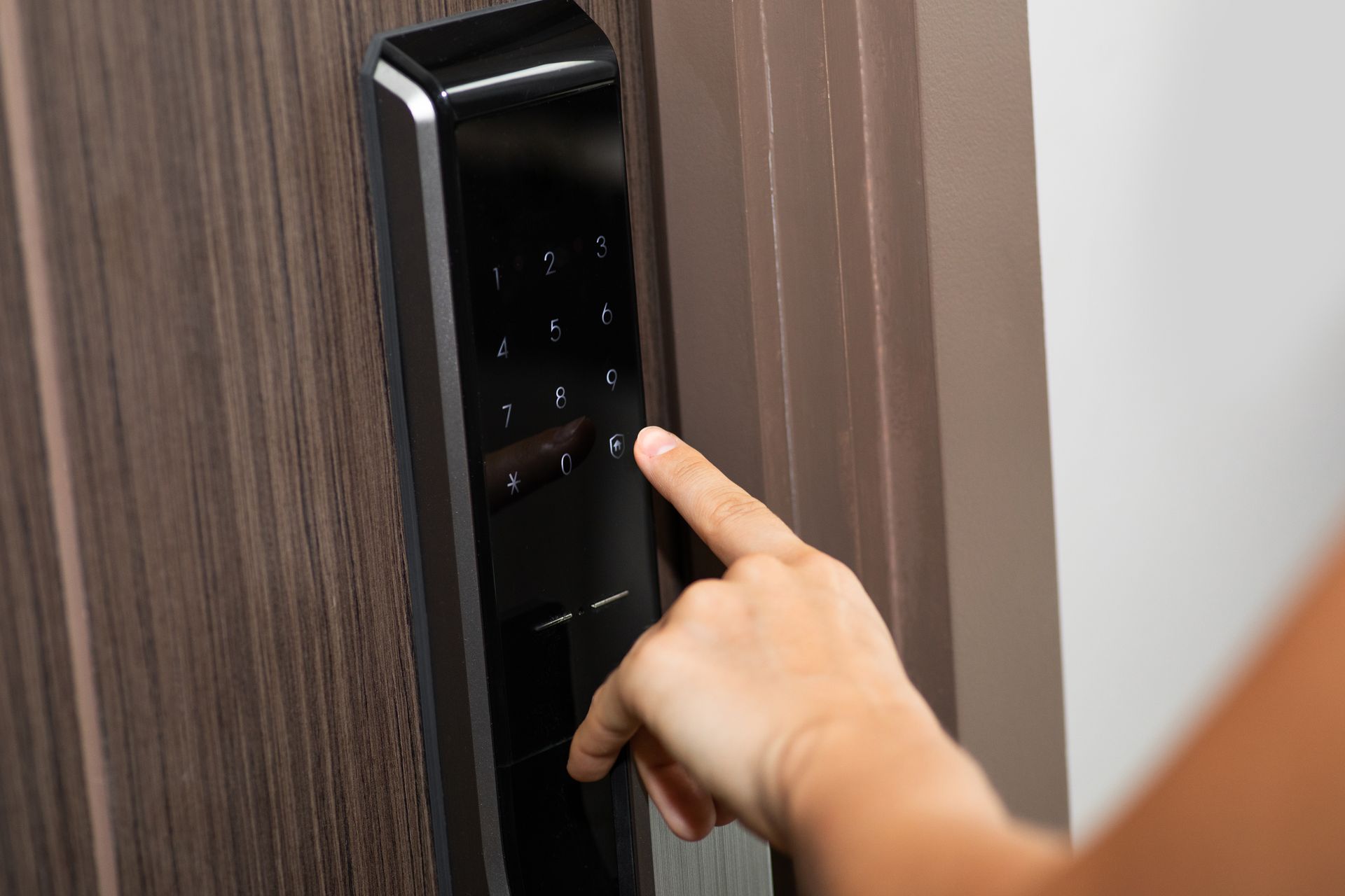 Person's finger pressing numbers on a black digital keypad door lock installed on a brown wooden door.