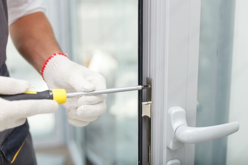 Person in gloves using a screwdriver to fix a white door lock.