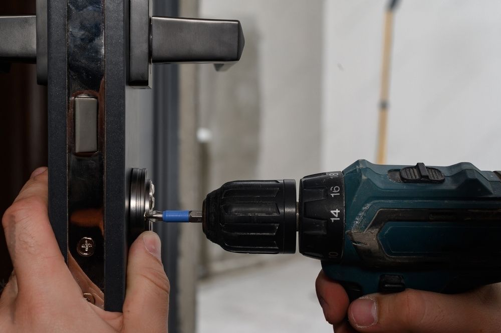 Person using a power drill to install a door lock. Close up on hands, door, and drill.
