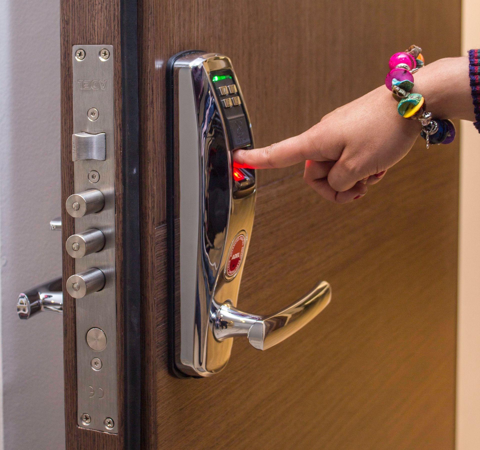 Fingerprint door lock being activated. Child's hand on a chrome handle; red light glows.