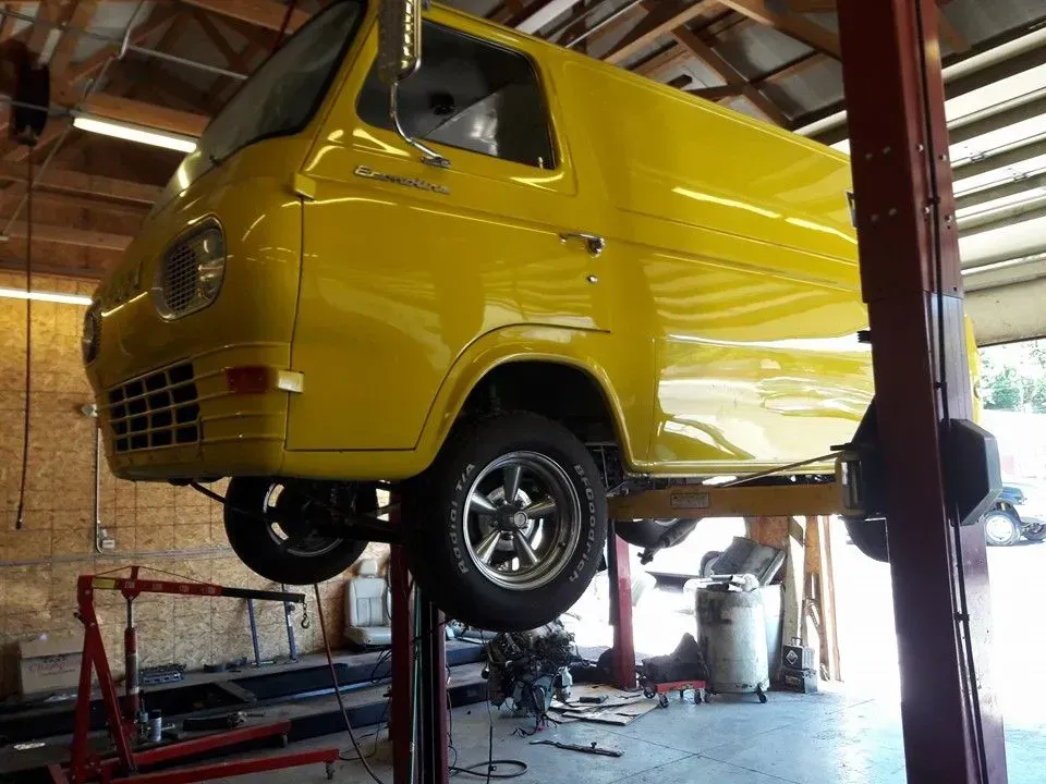 Yellow van lifted on a garage hoist inside an auto repair shop