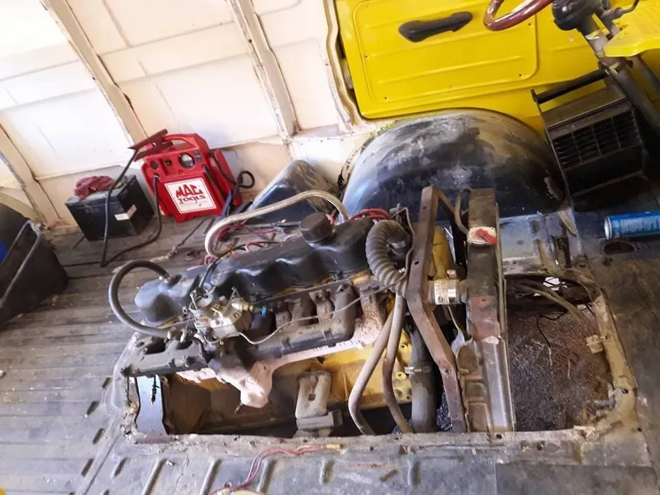 Engine compartment in a yellow vehicle body, with exposed mechanical parts in a workshop garage.