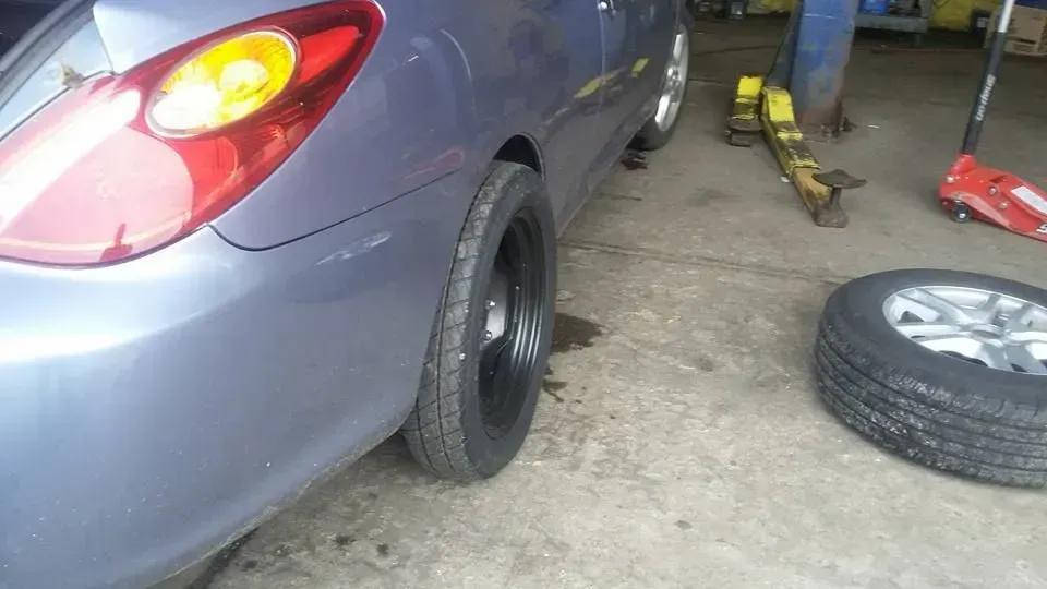Gray car with rear wheel removed in a garage, a loose tire and tools on the floor