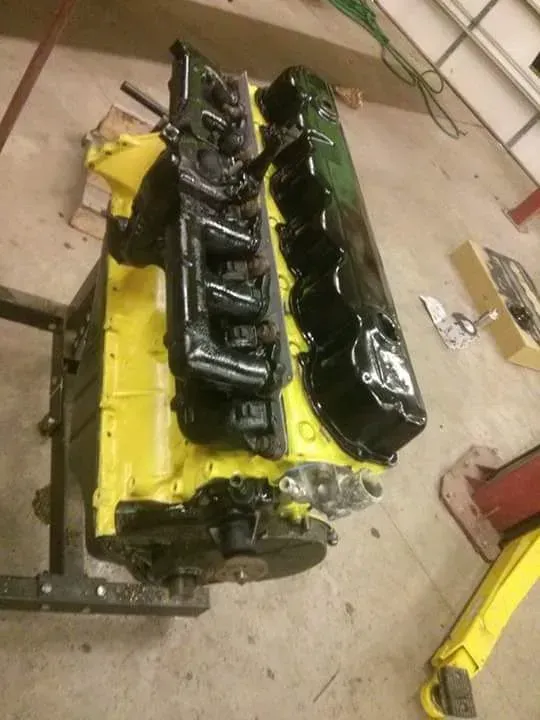 Yellow and black car engine block on a workshop floor, viewed from above.
