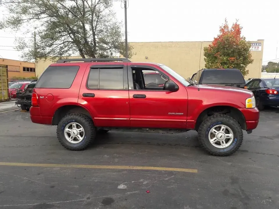 Red SUV parked in a parking lot with a beige building and trees in the background