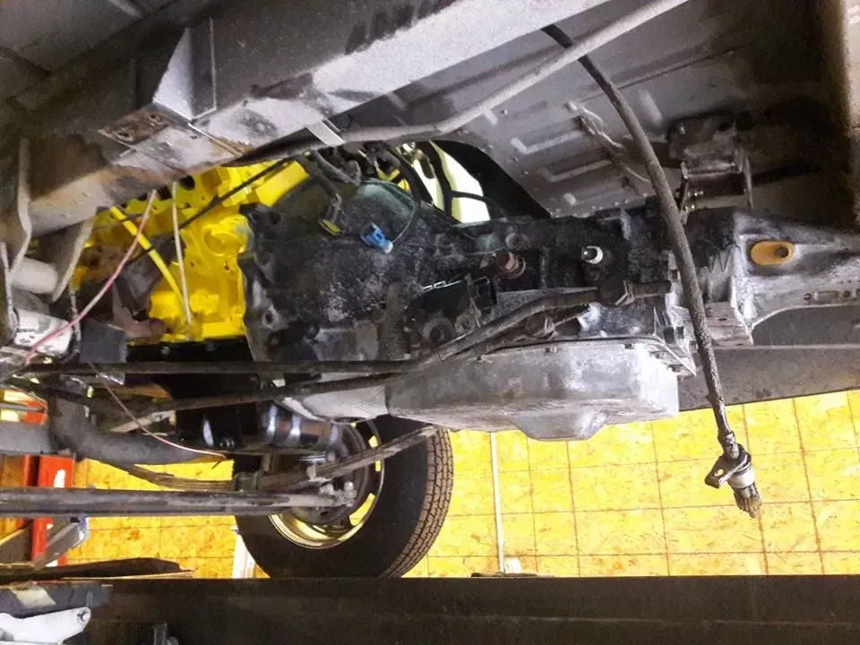 Undercarriage of a car on a lift, showing engine and suspension components with yellow lift arms