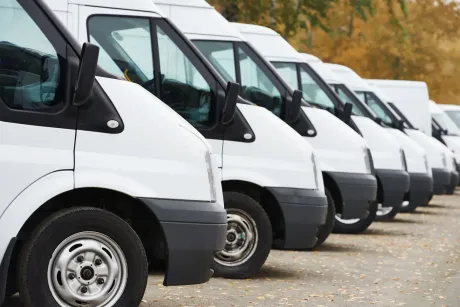 Row of white cargo vans parked side by side outdoors