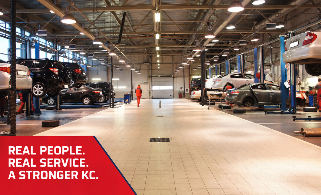 Auto service bay with cars on lifts and a worker in orange; red banner reads “Real People. Real Service. A Stronger KC.”