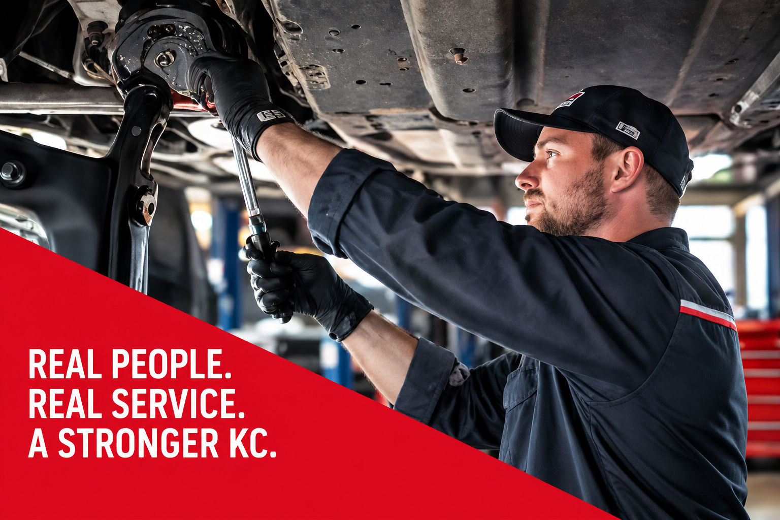 Mechanic inspecting a car's brake system in a shop, with red banner reading “REAL PEOPLE. REAL SERVICE. A STRONGER KC.”