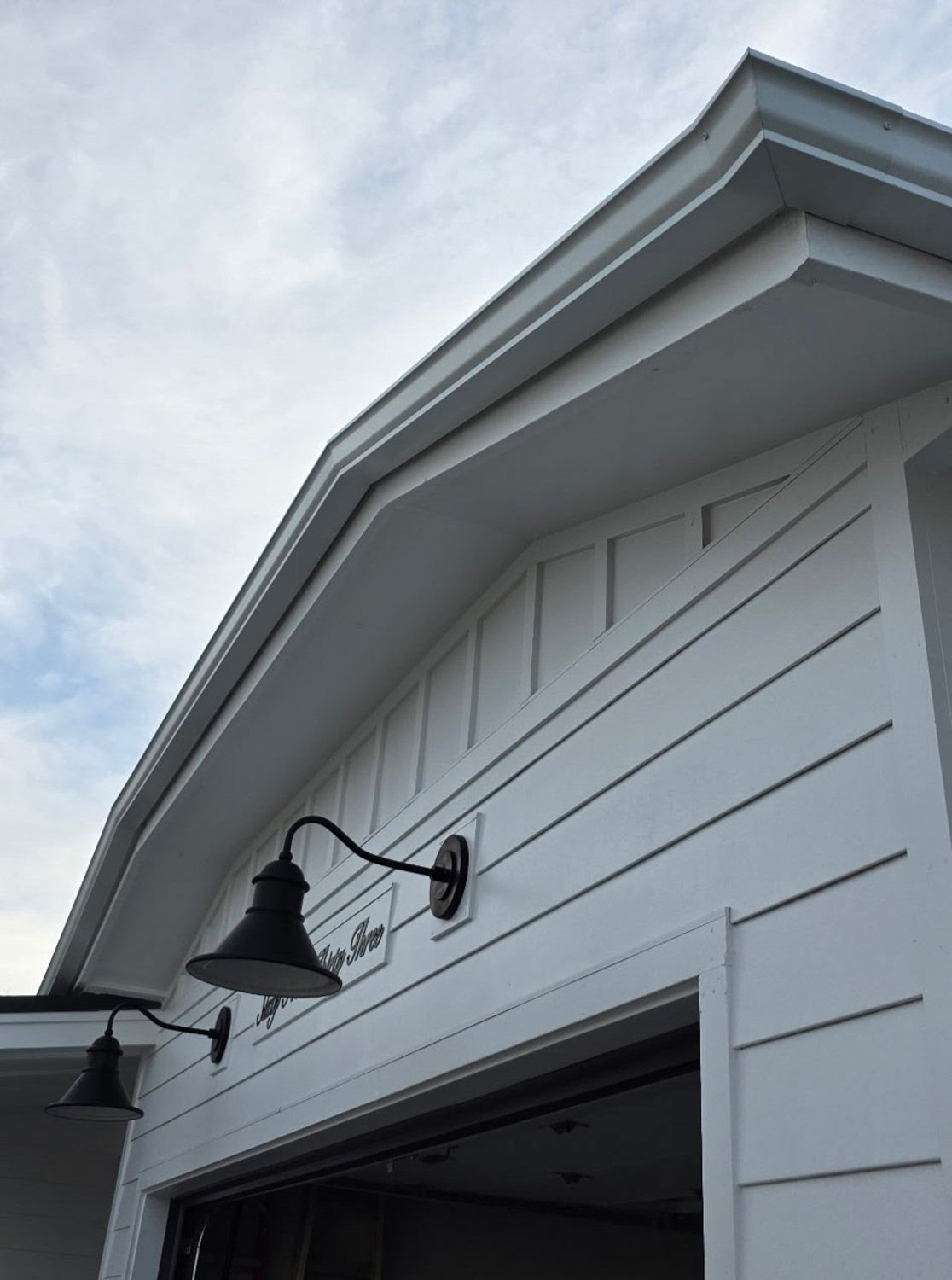 White building exterior with black gooseneck lights, angled roofline, and blue sky. New seamless gutters installed by Gutter Specialist in Reno, NV