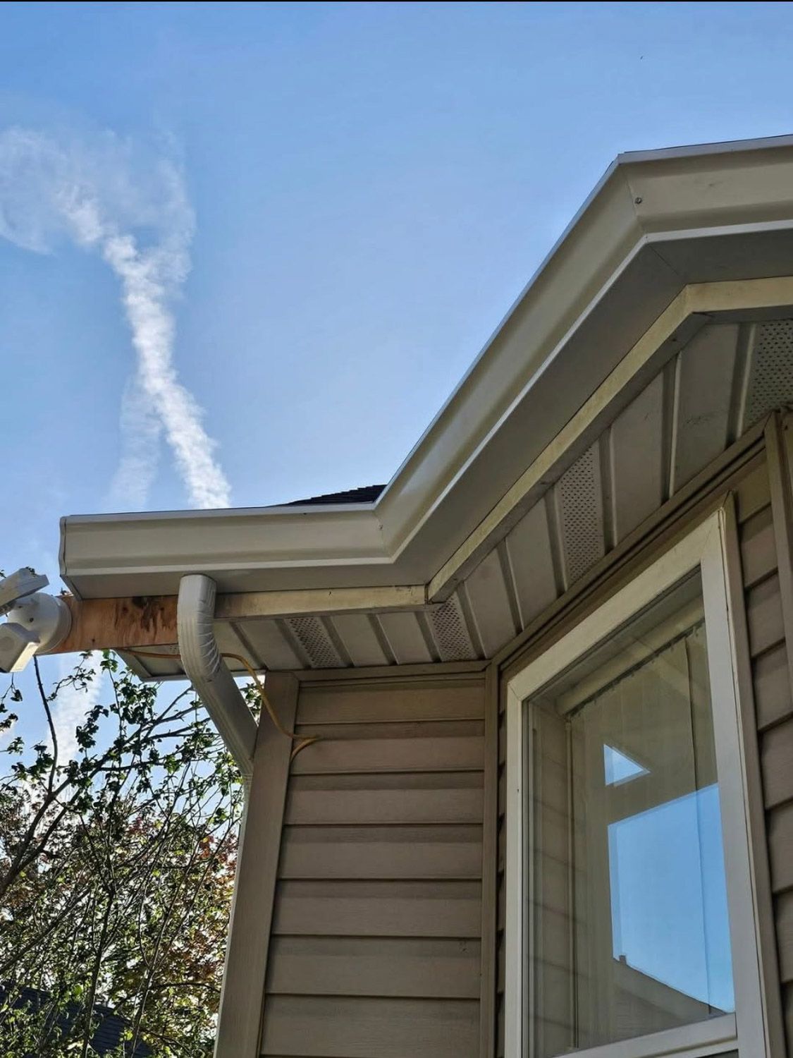 Tan house exterior with white gutters, a window, and a blue sky with cloud streaks.