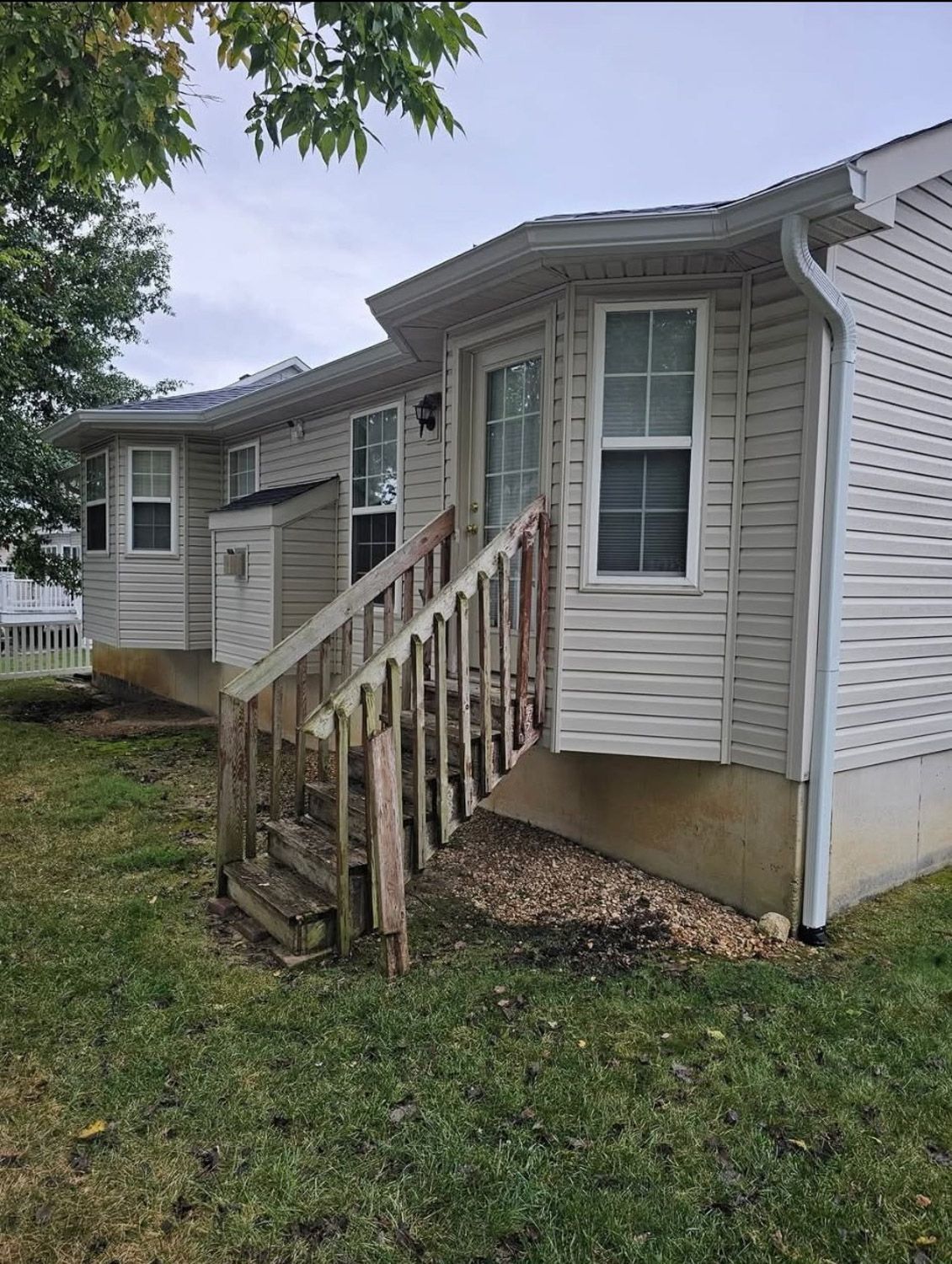 Exterior view of a house with wooden stairs leading to a doorway; siding is light-colored, overcast sky. New seamless gutters installed by Gutter Specialist in Reno, NV