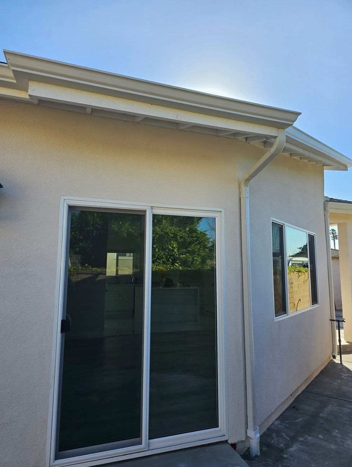 Exterior view of a stucco building with a sliding glass door and a window under a bright blue sky.New seamless gutters installed by Gutter Specialist in Reno, NV