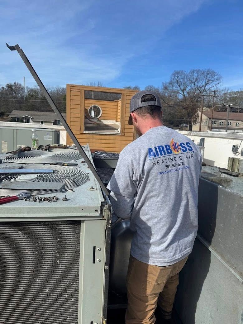A technician in a gray shirt works on an industrial HVAC unit on a sunny rooftop.