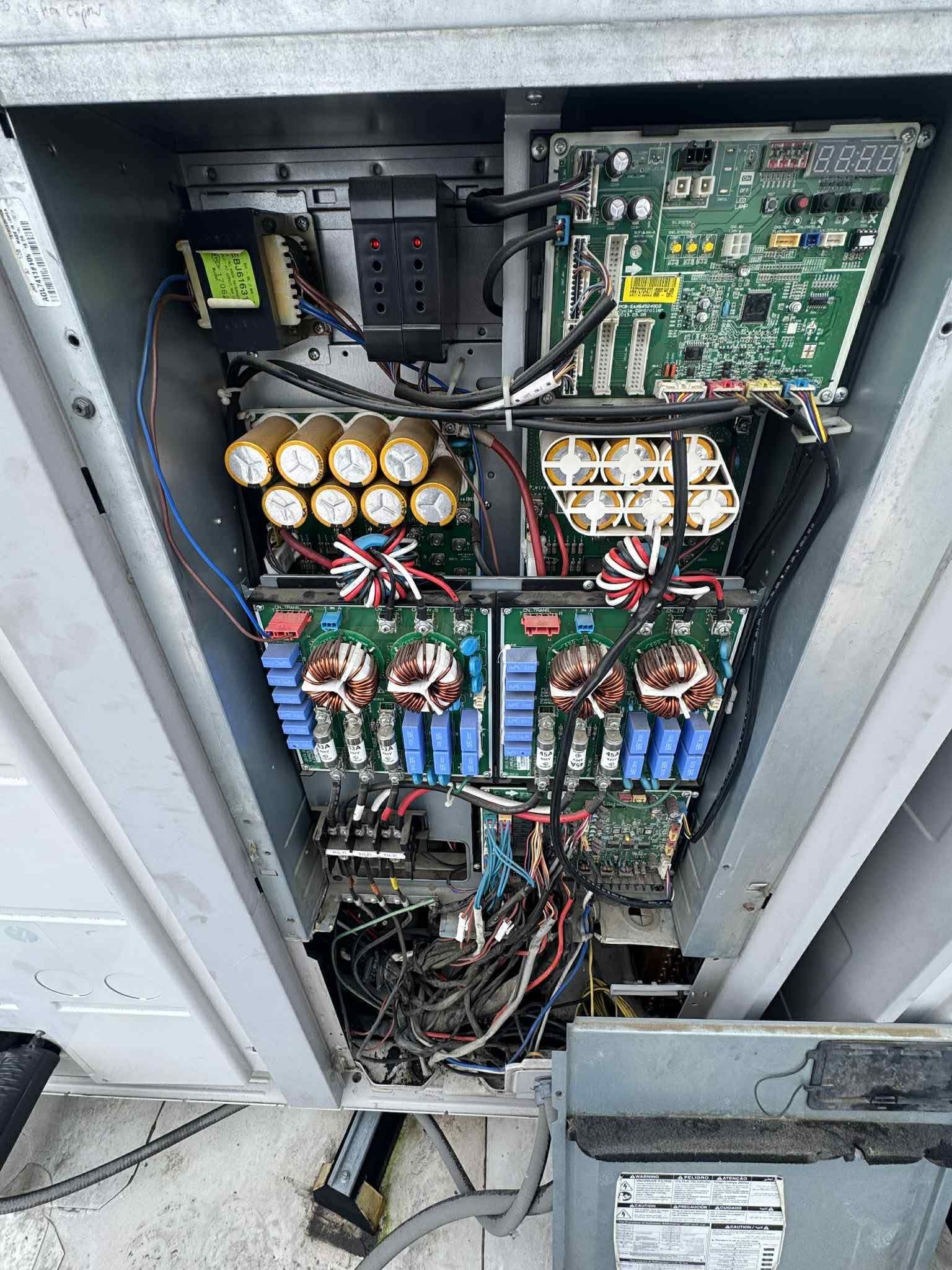 Open panel of a industrial HVAC control unit showing circuit boards, wiring, and capacitors inside a metal enclosure.