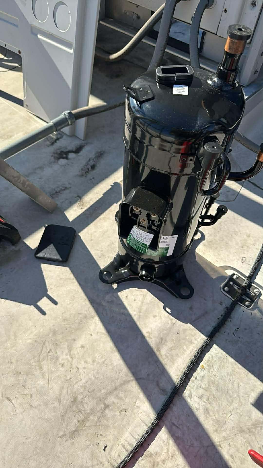 A black HVAC compressor stands on a rooftop with its electrical access panel open.