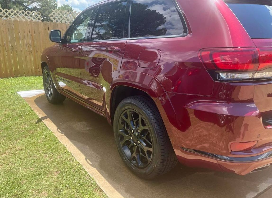 Maroon SUV parked on grass beside a wooden fence on a sunny day