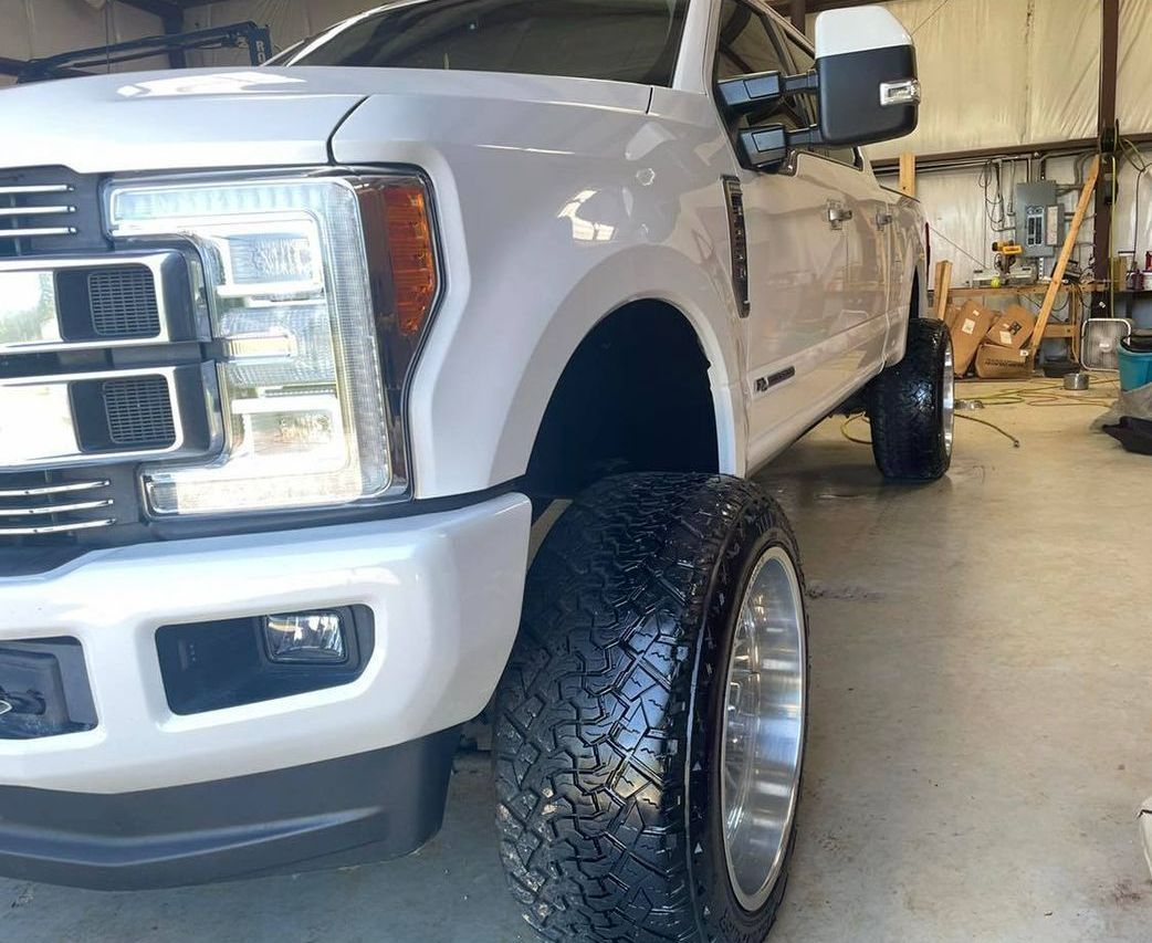 White lifted pickup truck in a garage, front-left view with large off-road tires.