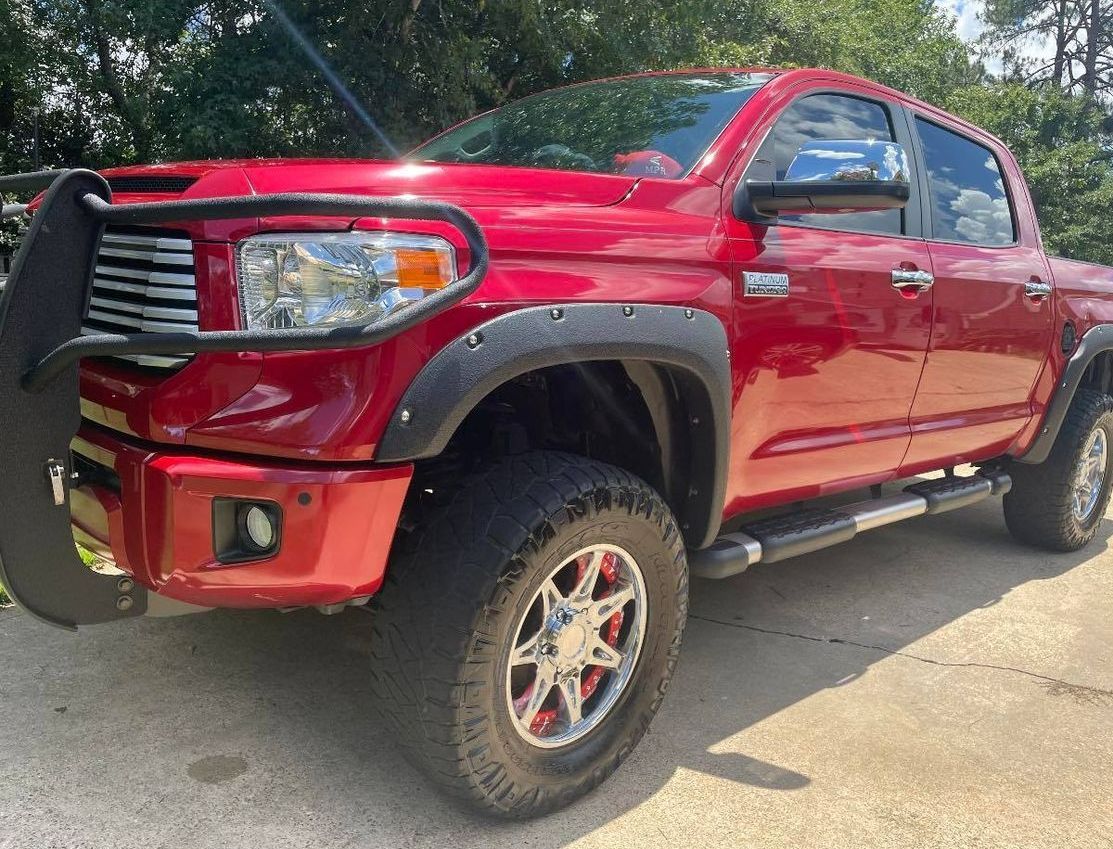 Red lifted pickup truck with black grille guard and off-road tires parked outdoors in sunlight