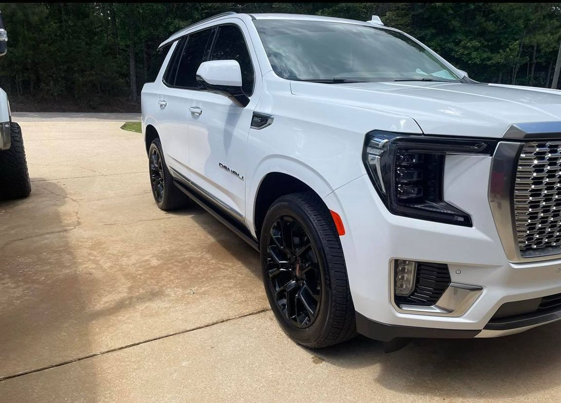 White GMC SUV parked on a driveway, angled front view with black wheels and chrome grille.