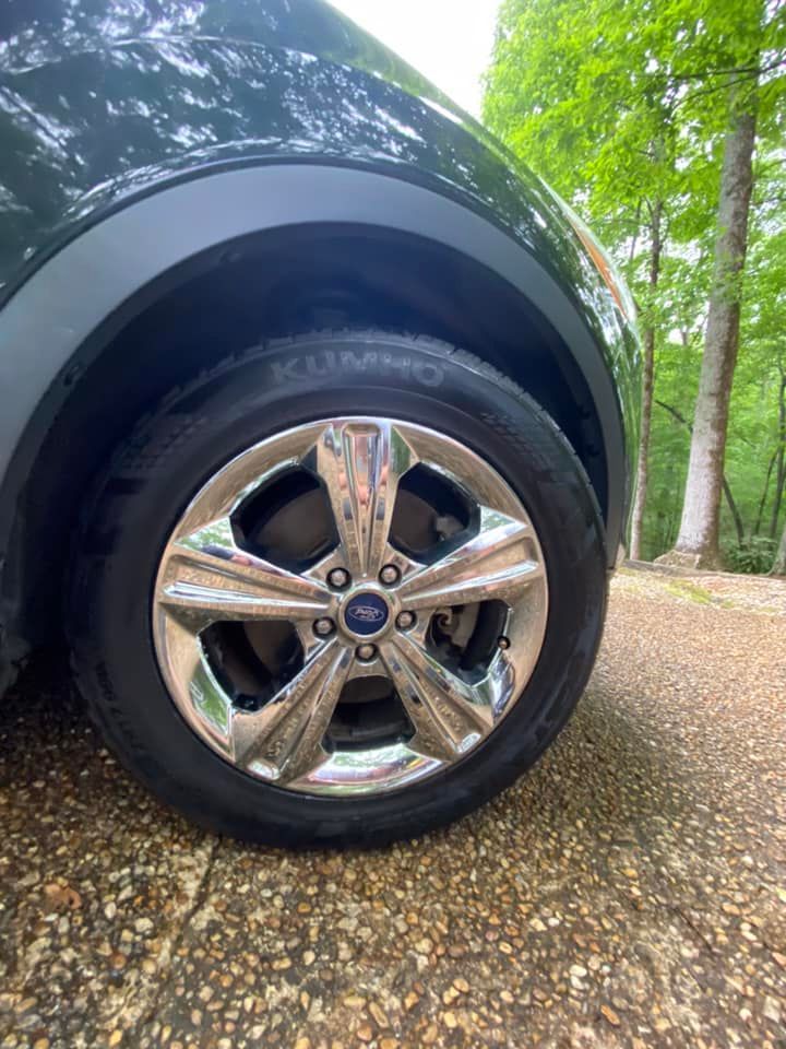 Close-up of a black SUV wheel with chrome rim parked on a gravel road beside trees