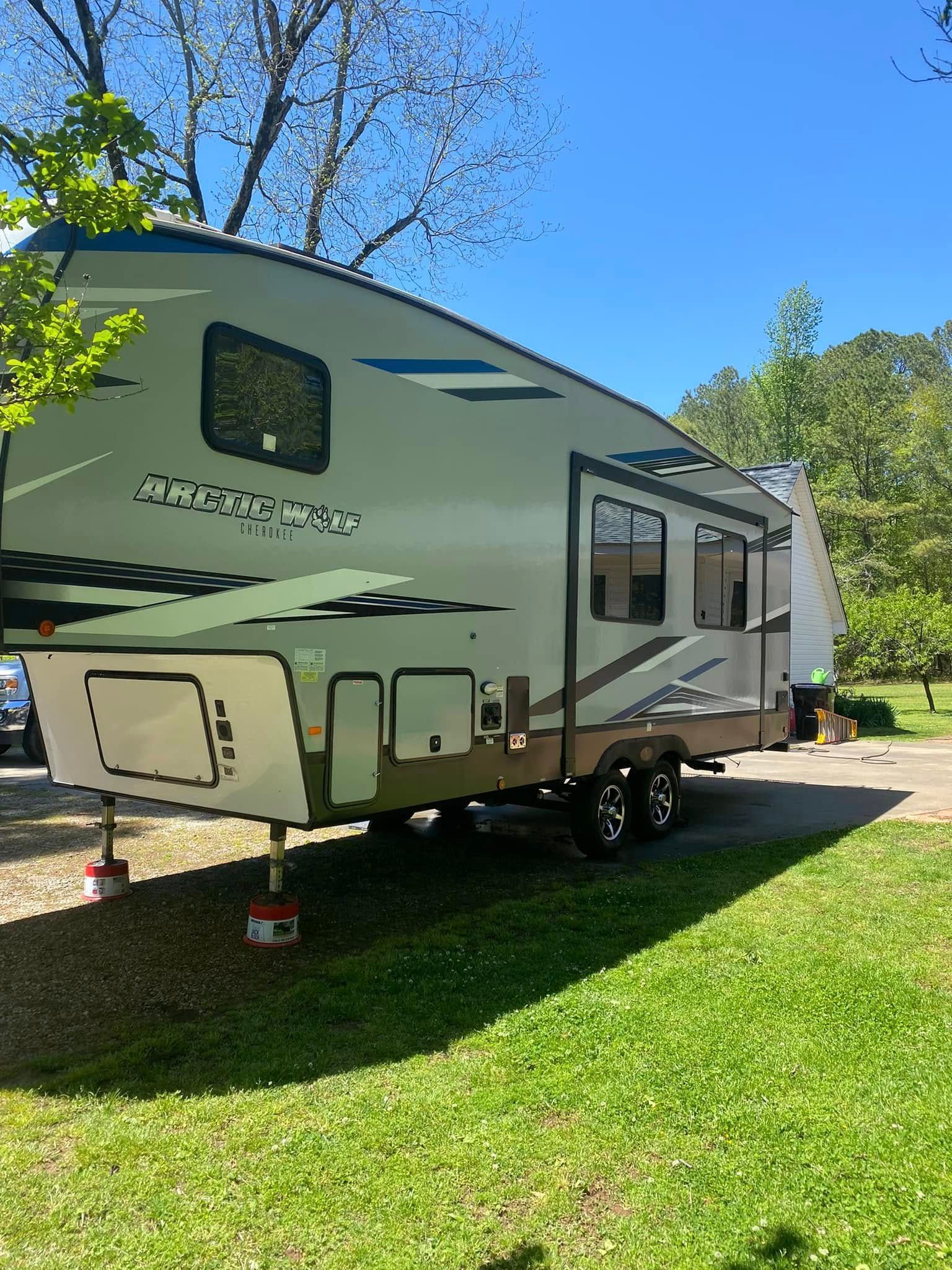 White fifth-wheel RV trailer parked on grass under trees on a sunny day